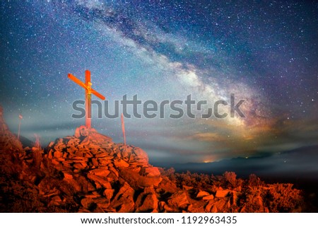 Cross on Mount Strymba wooden raised to the glory of God, Jesus Christ. Night light lighting a fire on a background of mountains alpine vegetation stones under the stars of the Milky Way