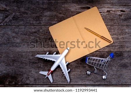 Empty brown notebook paper, pen, shopping cart and airplane model mock up design template isolated on wooden table background. Online shopping concept. Copy space for your text and design.