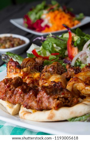 Turkish and Arabic Traditional Adana, Lamb and Chicken Kebab serving with salad, yogurt, onion, pepper, bulgur and parsley on rustic black wood table. Dark photography concept with copy space.