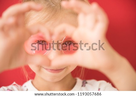 Little girl makes a heart shape in pink sunglasses on a red background