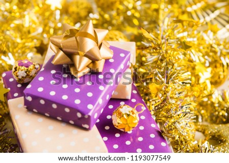 Elegant beige and violet (purple) gift boxes stack with ribbon with golden christmas decoration, New Year presents with golden garland and tinsel