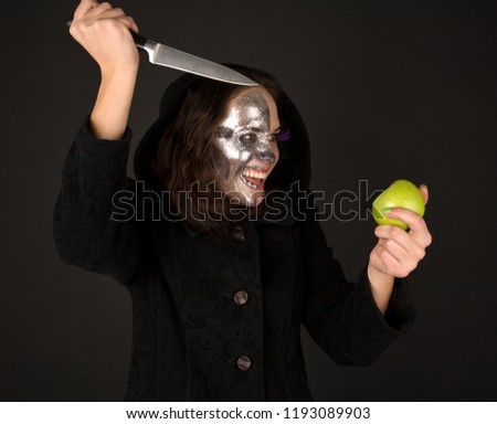 Picture of two-faced witch with green apple and knife screaming. Halloween makeup.