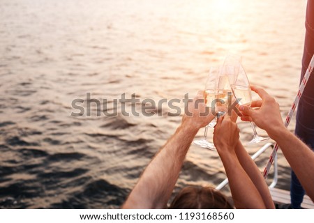 Nice picture of four hands holding glasses of champaigne in front of water. They have some rest. It gets darker. Sun goes down.
