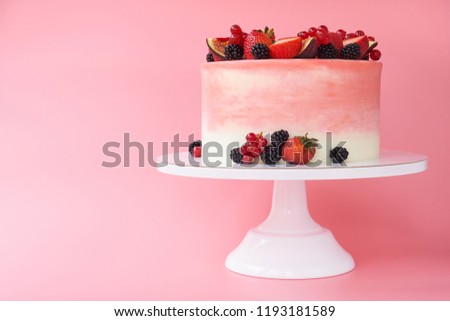 Cake with whipped pink cream, decorated with fresh strawberries, blackberry, figs and red currant on pink background. Picture for a menu or a confectionery catalog.