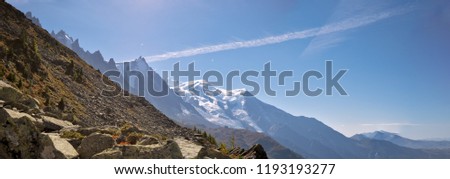 The  high peaks of the chamonix valley and Mont Blanc Massif in the village of Chamonix in France.  high alpine snow covered mountains surround the foreground rocks and alpine terrain.