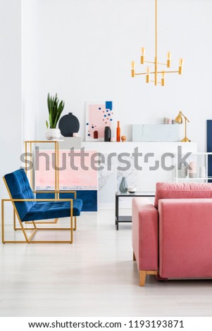 Vertical view of pink velvet couch and blue armchair in living room fool of paintings and maps, real photo