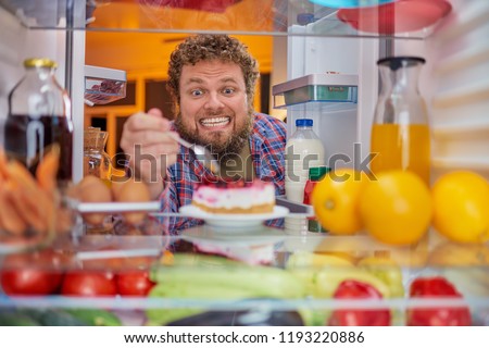 Man eating cheesecake. Unhealthy eating concept. Picture taken from the inside of fridge full of groceries.