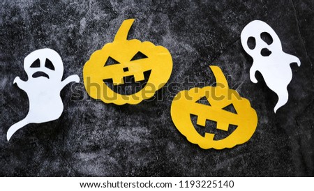 Halloween concept with pumpkins and ghosts cut paper on black concrete background.