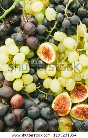 Red globe and green  grapes on a wooden cutboard and figs over a white background, top view,natural light,  space for text.