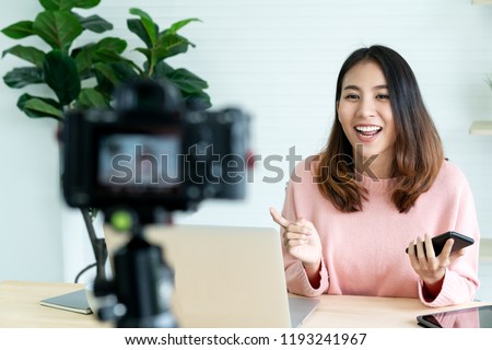 Young attractive asian woman blogger or vlogger looking at camera and talking on video shooting with technology. Social media influencer people or content maker concept in relax casual style at home. Royalty-Free Stock Photo #1193241967