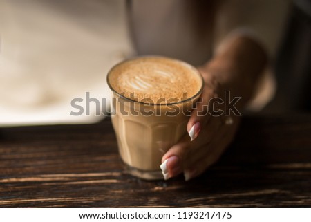 female hands with beautiful manicure close-up hold a cup with hot coffee on a wooden table