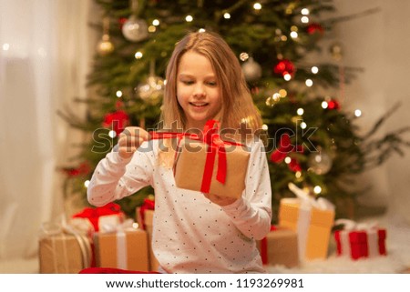 christmas, holidays and childhood concept - smiling girl with gift box at home