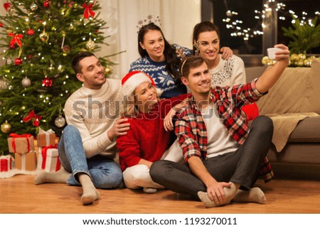 celebration and holidays concept - happy friends with glasses celebrating christmas at home party and taking selfie by smartphone