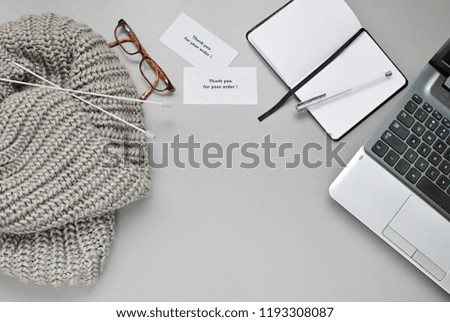 Handmade knitted scarf, knitting needles, laptop, notebook, Thank you for order cards on gray background, copy space, flat lay, work at home concept, selling handmade items online.