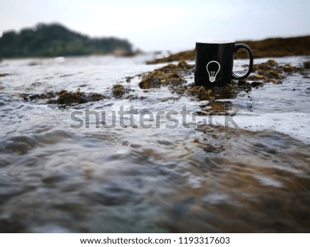 An idea sign on a black mug. Selectively focused mug with background of sea nature (bokeh)