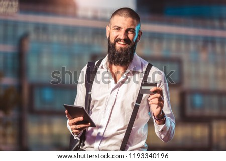 Portrait of a young caucasian businessman holding a tablet and credit card outdoor