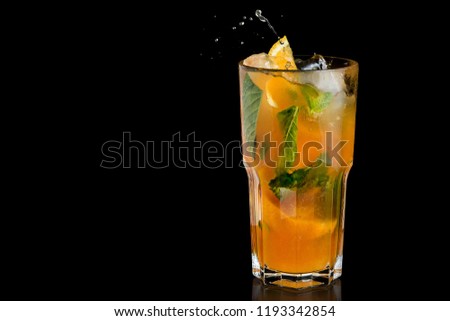Fresh orange lemonade with mint leaves. Beverage splash on black background.