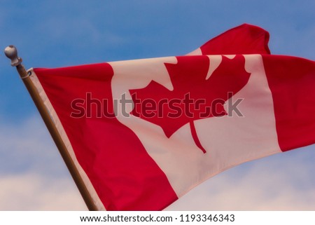 Beautiful red and white Canadian flag with a maple leaf waving brightly in the wind and sunshine with a blue sky’s and clouds Royalty-Free Stock Photo #1193346343