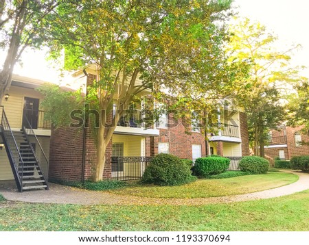 2-story apartment complex building in suburban North Texas, America in fall season sunset. Grassy lawn patio yard and autumn yellow dry leaves falling on the pathway near metal staircase