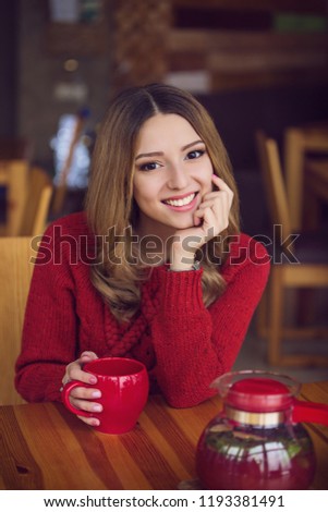 beautiful happy girl in a red sweater sits in a cafe with a cup of tea