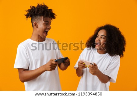 Image of excited young cute african couple isolated over yellow background play games by mobile phones.