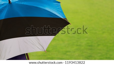 Estonia flag umbrella. Close up of printed umbrella over green grass lawn /field. Rainy weather forecast concept.