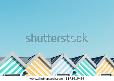 Light blue sky background and top roofs of colourful striped beach huts and copy space above