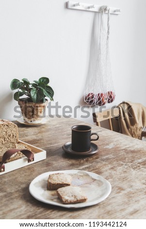 Vintage interior design of kitchen space with wooden table against white wall with simple chairs,  scarf, cups of coffee and breakfast. Minimalistic concept of kitchen space.