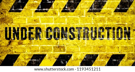 Under construction warning sign with yellow and black stripes on brick wall texture background in wide panorama format. Concept for do not enter the area, caution, danger, construction site.