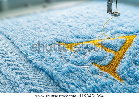 Close up picture embroidery design yellow alphabet monogram A on blue towel embroider by machine, copy space on the left side.