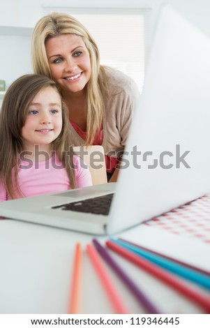 Mother standing behind daughter looking at laptop in kitchen