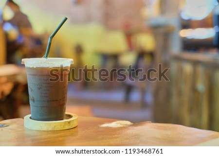 Black ice coffee in plastic glass on old wooden table in cafe, yellow background