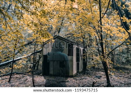 A ghostly hooded figure standing next to an eerie disused hut in a woodland in autumn