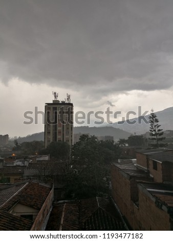 A storm rain is coming over the city of Medellin, Colombia. Tenebrous gray sky with large black clouds. Haze and cold feeling over brick houses.