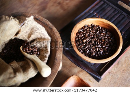 Many coffee beans placed around on a wooden dish in a warm on wood background. light atmosphere, on dark background, with copy space.