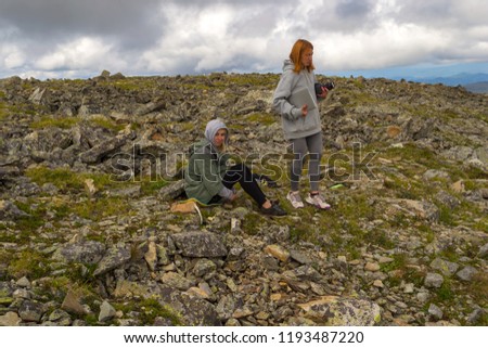 Two girls on the top of the mountain rest during the ascent of the mountain of the Altai in sport clothes with laptop in the arm on the background with a lot of stones and big clouds in the sky
