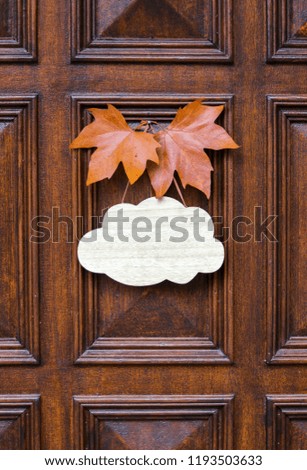 Mock up, welcome empty table sign of cloud shape decorated with two orange maple leaves hanging on dark wooden entrance door. Welcome autumn. Copy space