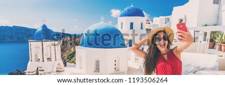 Happy tourist taking selfie having fun on Europe summer vacation in Santorini, cruise destination panoramic banner. Asian woman funny holding mobile taking picture.