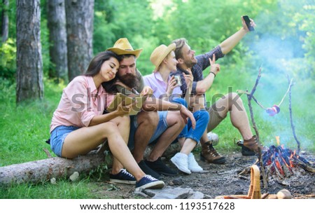 Tourists sit log near bonfire taking photo on smartphone. Friends on vacation capture moment. Friends near bonfire enjoy vacation and roasted food. Man taking photo near bonfire nature background.