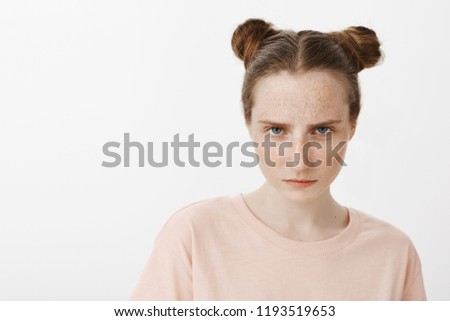 Girl looking at enemy, feeling scorn and anger, looking from under forehead at camera and frowning, standing serious and outraged over gray background, having bad day in school Royalty-Free Stock Photo #1193519653