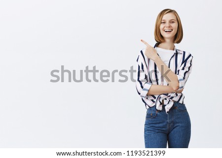 Proud of my ahievements. Good-looking successful european woman with short trendy hairstyle in striped blouse, smiling broadly at camera with confident expression and pointing at upper left corner