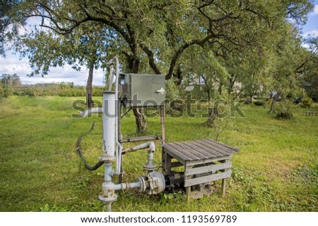 Old electric pump in a village on green grass.