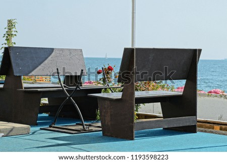 brown wooden chairs and a table with a red rose against the background of the sea