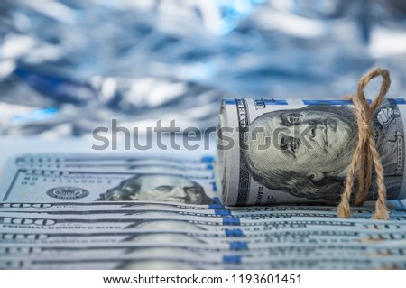 Against the backdrop of a hundred dollar bills spread out, the bundle of dollars is pulled with a rope.