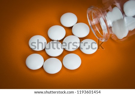 White tablets are scattered from a glass bottle on a yellow background. Vignetting
