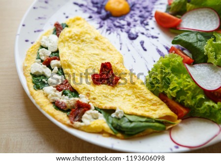 Delicious omelette for brunch in cafe. Tasty natural lunch food with natural ingredients. Fried eggs, dryed tomato, spinach and Greek feta cheese served on white plate in restaurant