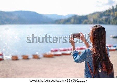 Young tourist girl taking picture with her phone at lake Titisee-Neustadt in the Black Forest,Germany.Woman backpack on vacation