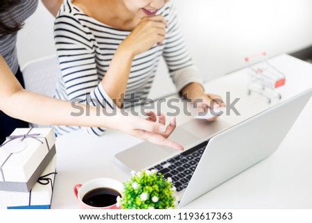 Two excited roommates friends shopping online with credit card and laptop on a couch in the living room at home with a window in the background