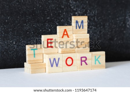 Wooden blocks with letter on white table on the blackboard background. Word 'TEAMWORK' on wooden tiles.