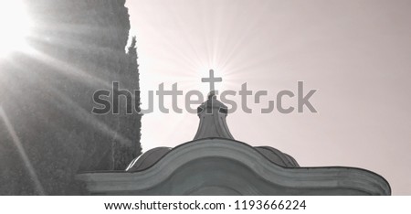 Cross on the top of the old chapel in cemetery with sun rays from left and lightening through the cross